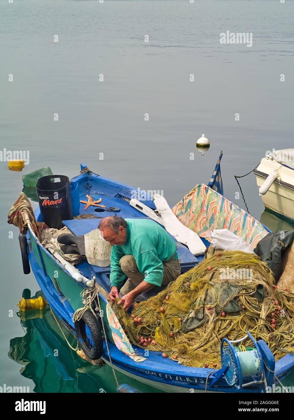 Kavala, Macedonia / Greece - May 14, 2019: Fisherman working on his fishing nets in traditional weathered blue wooden boat in the port of Kavala. Stock Photo
