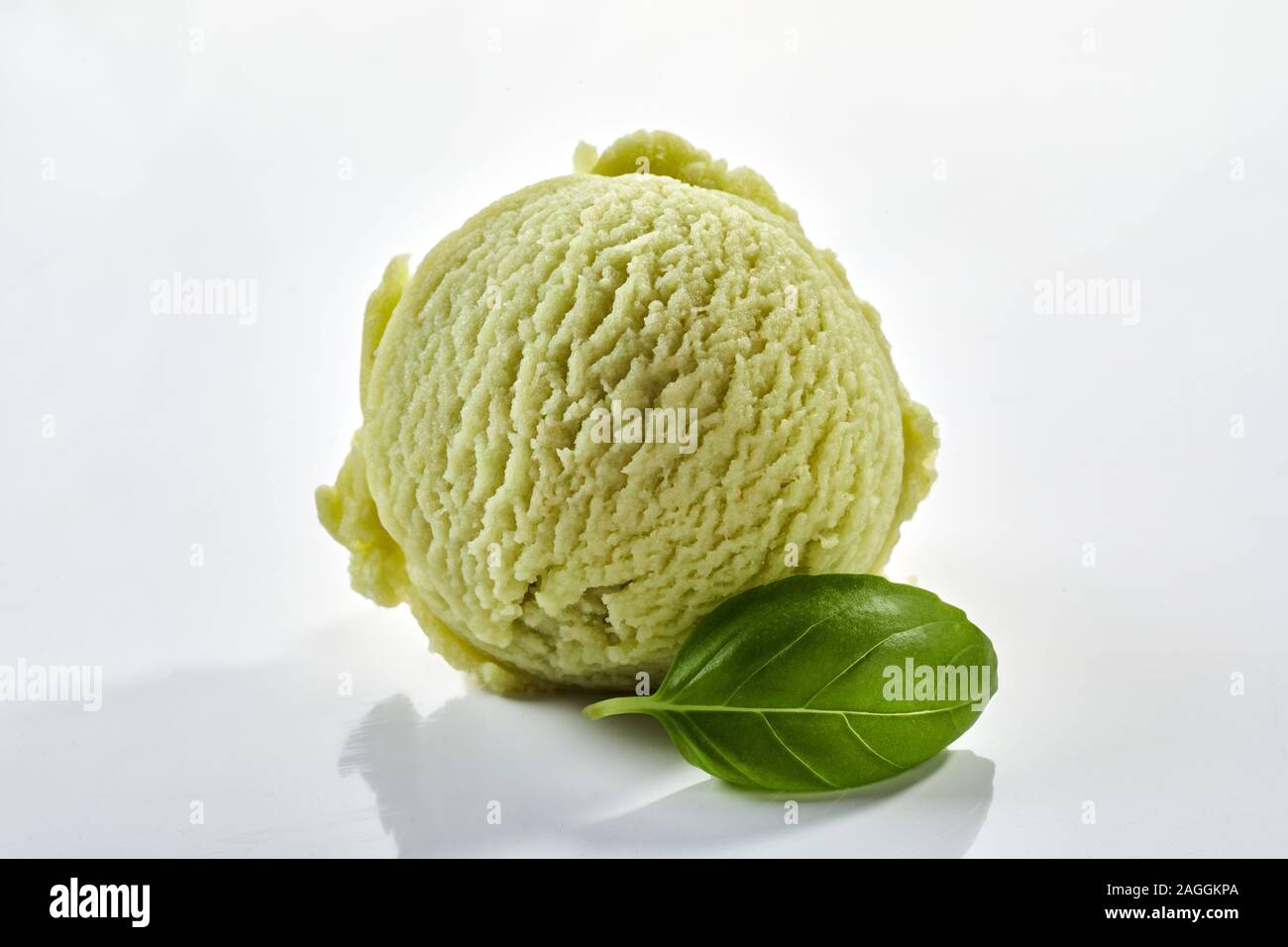 Single scoop of speciality herbal basil ice-cream with a fresh green leaf on a white background with shadow in close up Stock Photo
