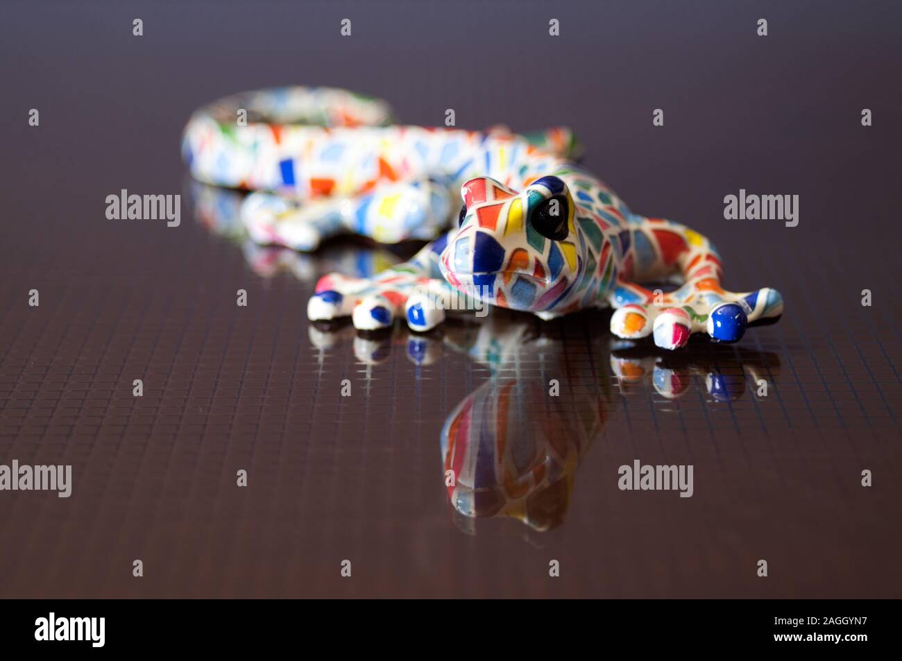 colorful designer lizard on a glass table. Reflex textured glass table. Colourful ceramic model salamander. Stock Photo