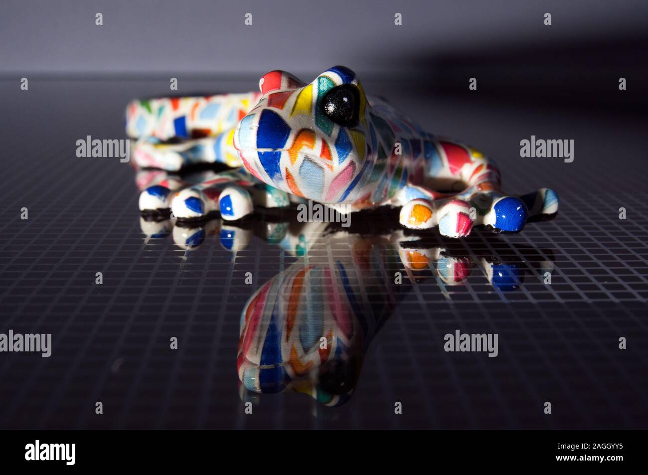 colorful designer lizard on a glass table. Reflex textured glass table. Colourful ceramic model salamander. Stock Photo