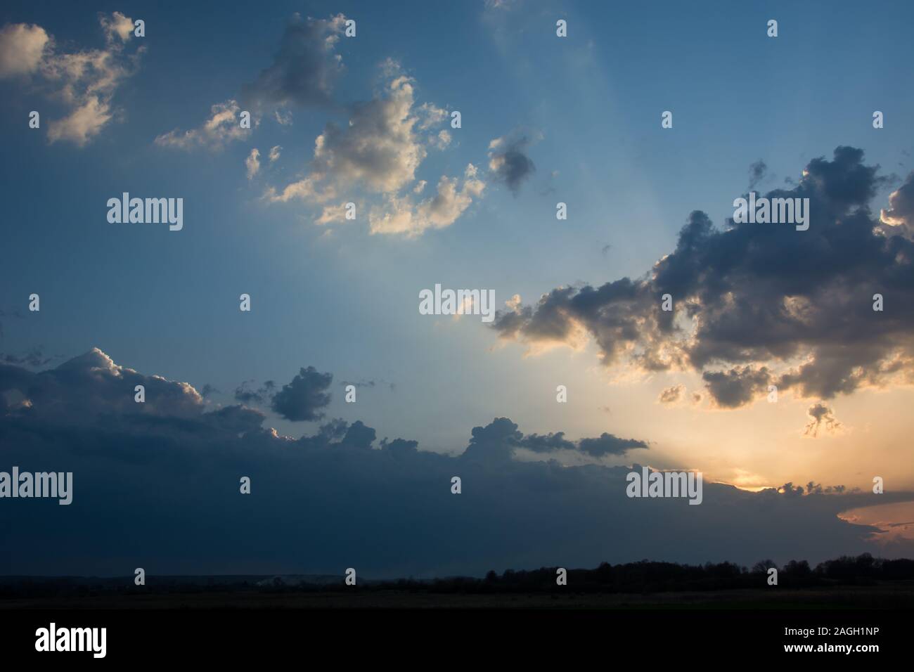 The sun setting behind clouds and sunrays above the horizon and colorful sky - evening view Stock Photo