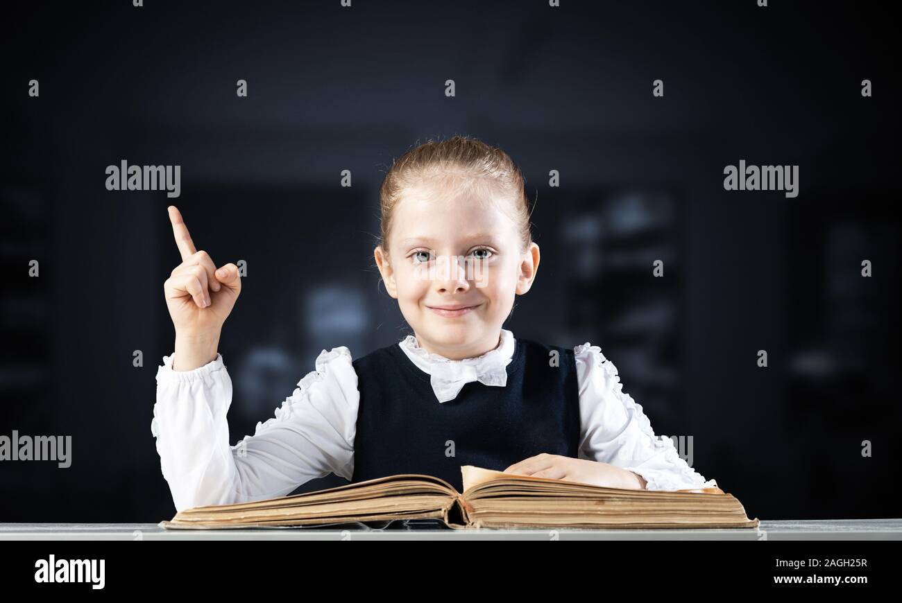 Smiling little girl sitting at desk with open book Stock Photo - Alamy