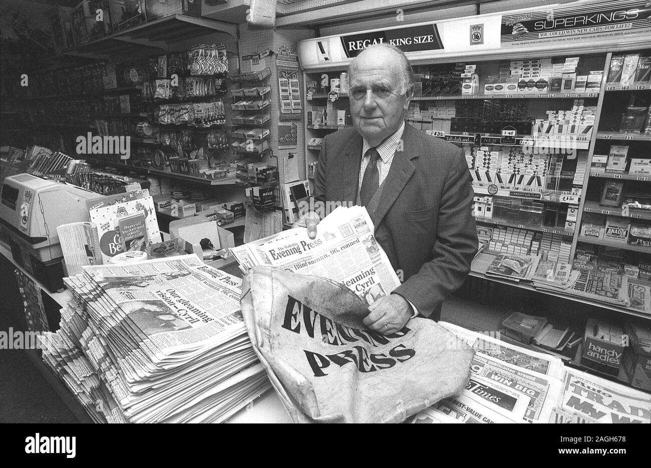 1980s, historical, a newsagent at the counter of his shop putting local evening newspapers into the delivery boy's papersack, Yorkshire, England, UK. Stock Photo