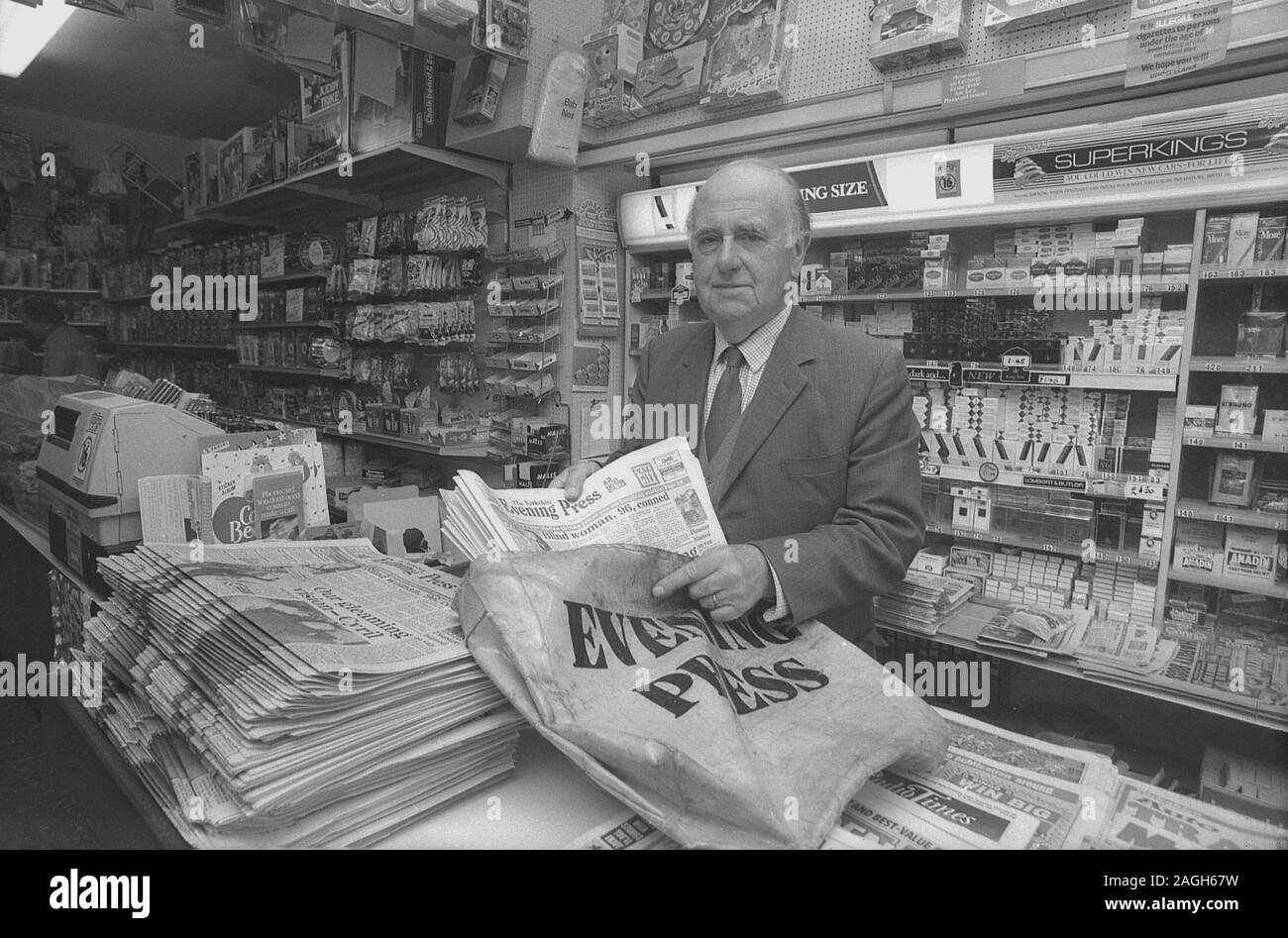1980s, historical, a newsagent at the counter of his shop putting local evening newspapers into the delivery boy's papersack, Yorkshire, England, UK. Stock Photo