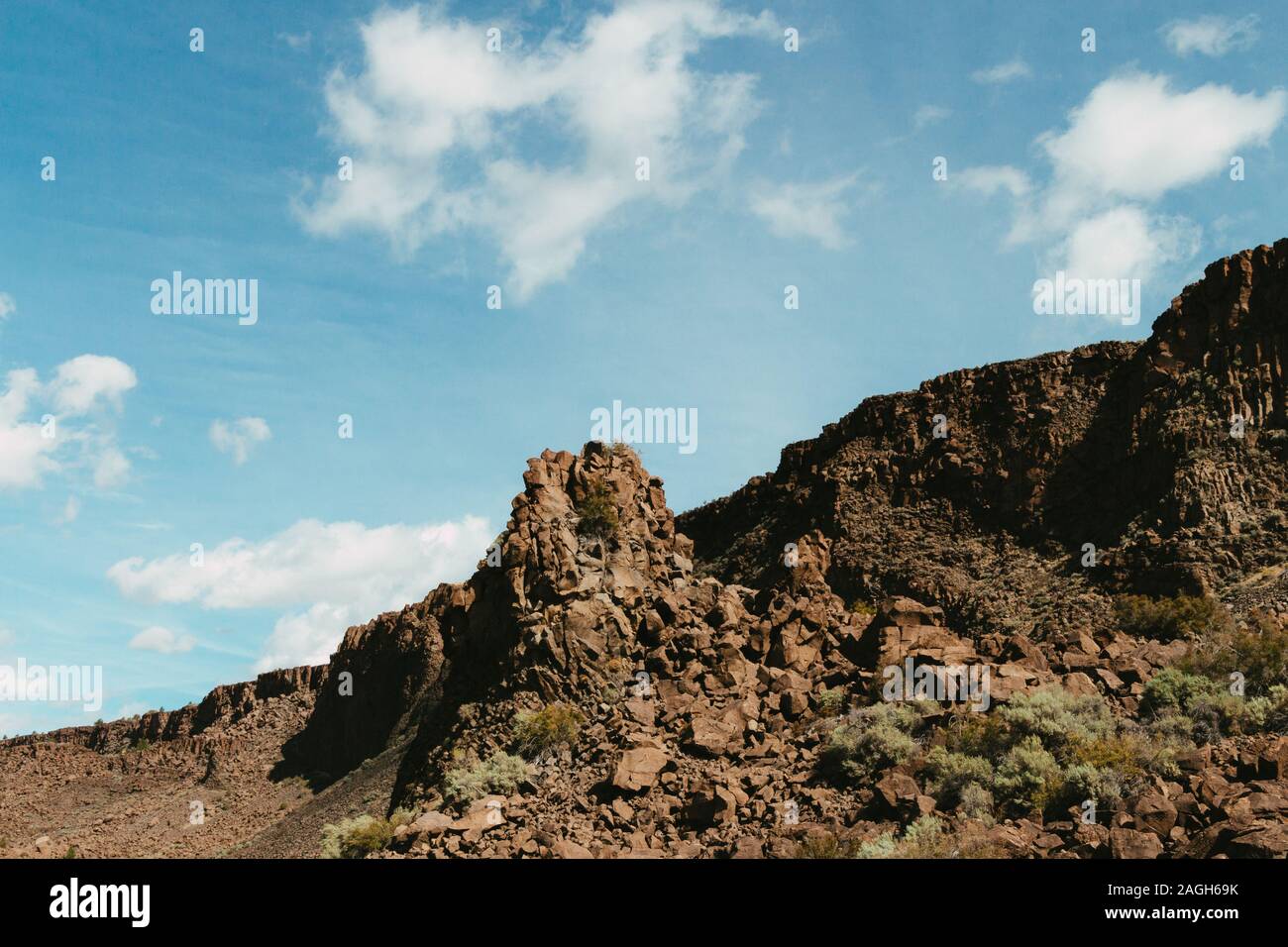 Landscape of rocks covered in greenery and dust under a blue cloudy sky ...