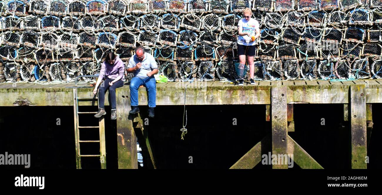 GONE FISHING - Fishing with hand lines on the pier at Dock End, Whitby, Yorkshire, UK with crab pots behind (in 2017) Stock Photo