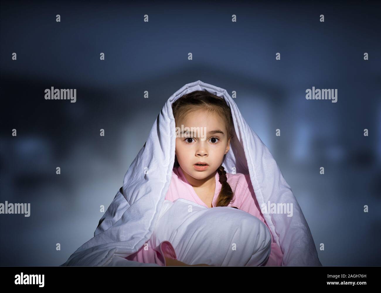 Scared girl with pillow hiding under blanket Stock Photo