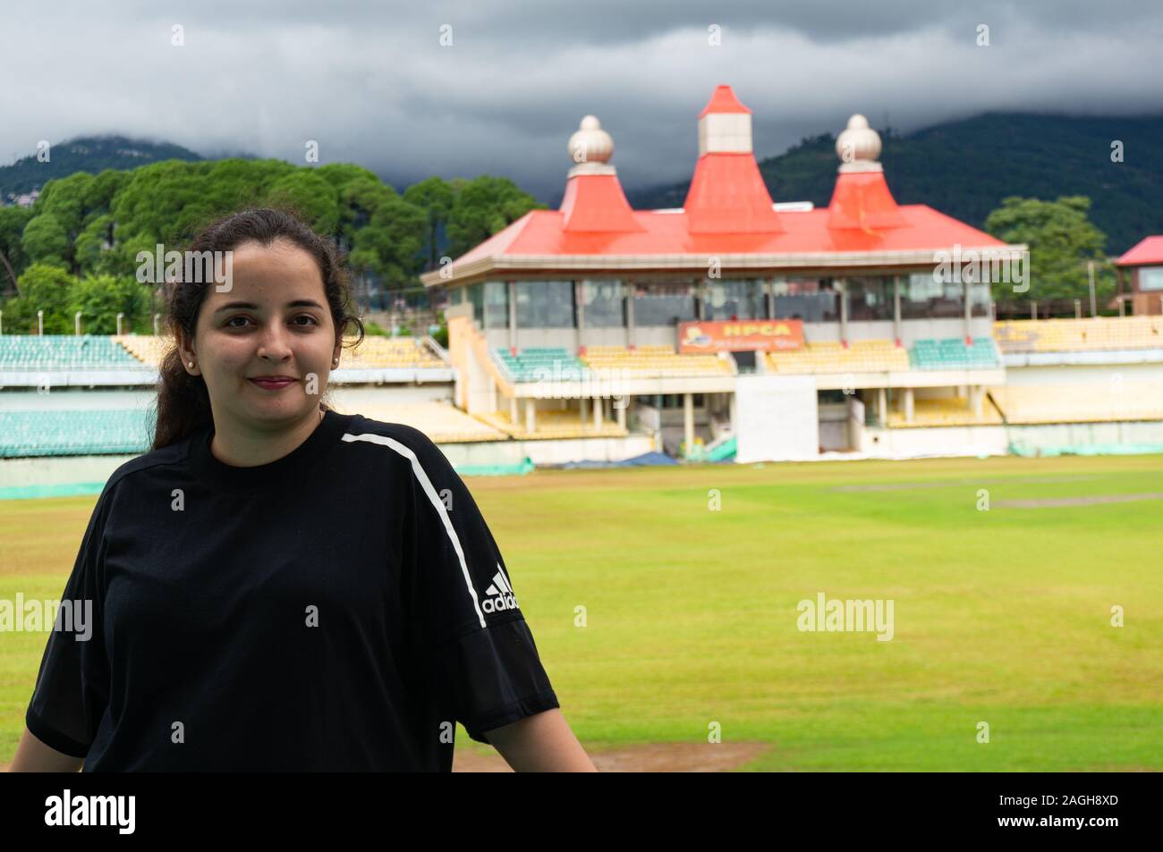 Young indian woman wearing black shirt standing at the iconic cricket stadium in dharamshala Stock Photo