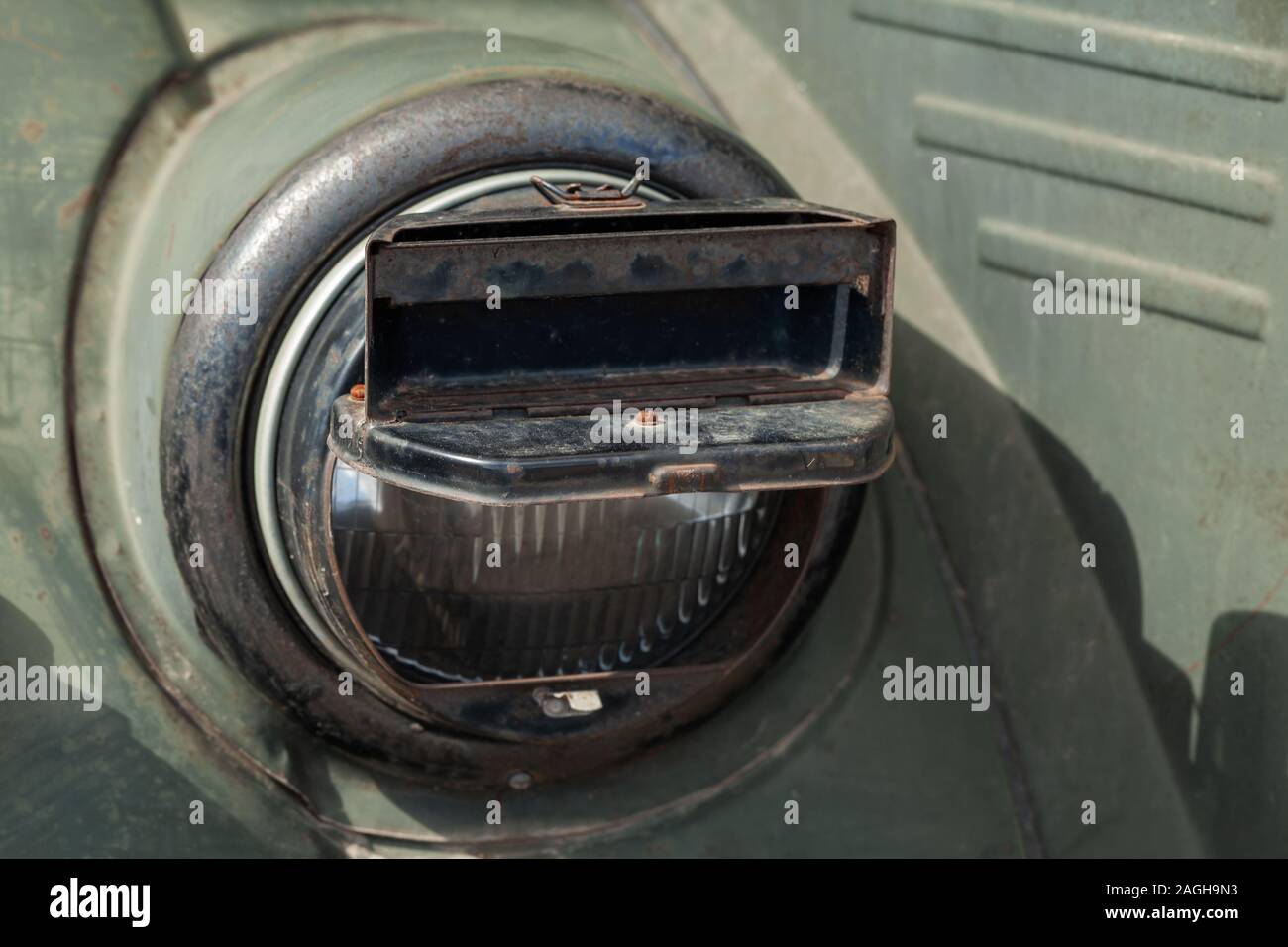 Round headlight of a military car with blackout headlight cover on it, old-timer vehicle from WWII period. Close up photo Stock Photo