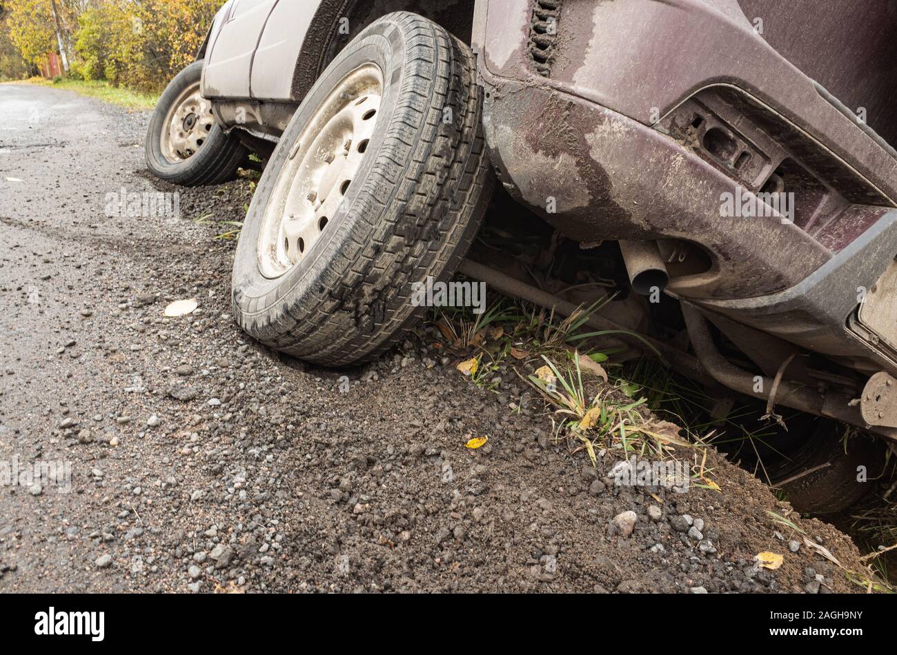 A car in an accident lies in a ditch by rural road at daytime, close up photo of rear bumper and wheel Stock Photo