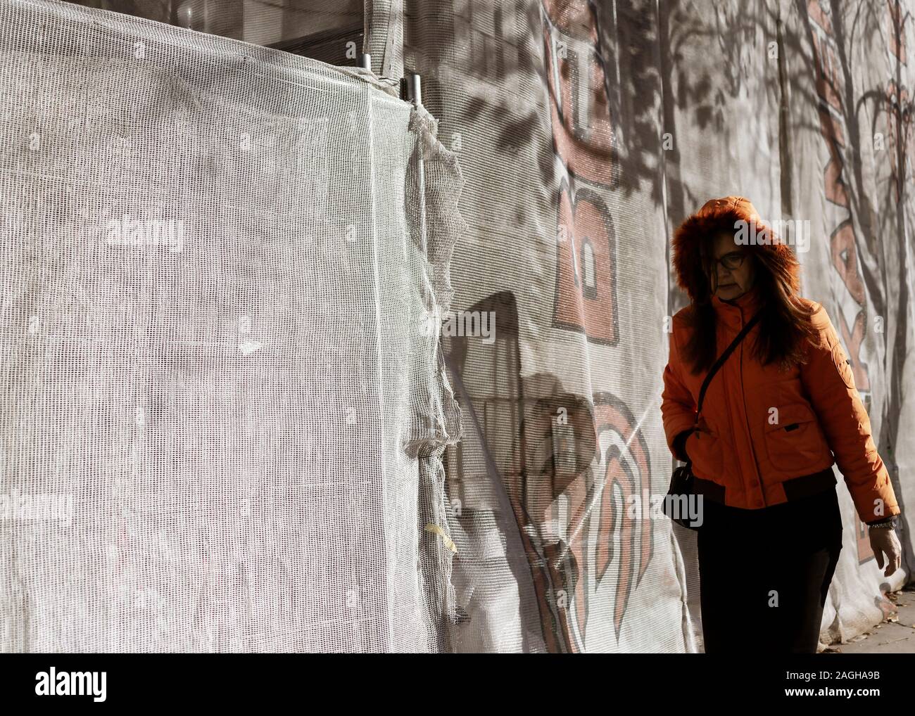 Belgrade, Serbia, Nov 24, 2019: A woman walking down the street next to a scaffold covered wall Stock Photo