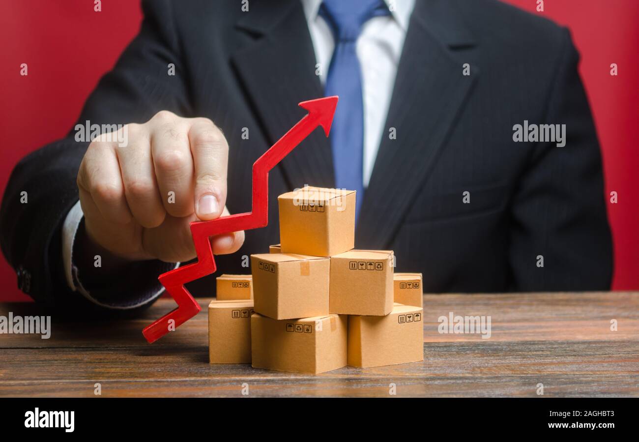 Businessman holding a red arrow up over boxes. Increase sales rate, industrial goods production volumes growth , expanding export opportunities, findi Stock Photo