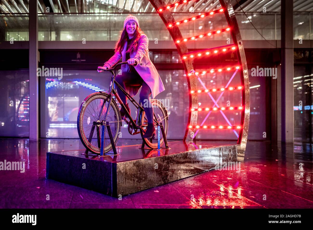 London, UK. 19th December, 2019. IlluminoCity exhibition by Light Art Collection. Student Jasmine Cook, 19, rides 'Lightbattle X' installation, a unique interactive bicycle light-artwork designed by Venividimultiplex, part of IlluminoCity exhibition in Principal Place, Shoreditch. Credit: Guy Corbishley/Alamy Live News Stock Photo