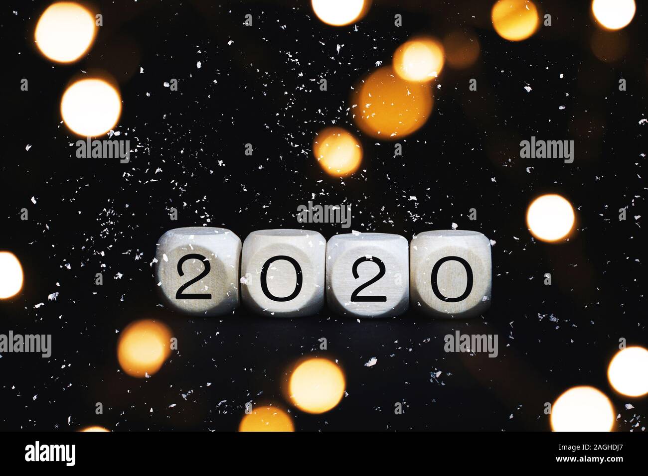 Wooden cubes with 2020 numbers on a black background. Christmas concept greeting card with blurred bokeh lights and snow. Stock Photo