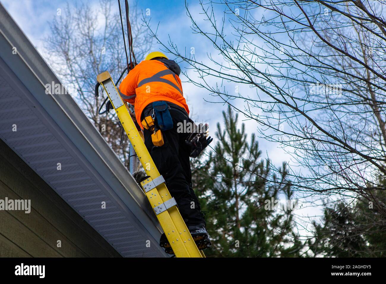 A domestic fiber optic installation is in progress as a workman is seen in full personal protective equipment, PPE, working at height from a ladder Stock Photo