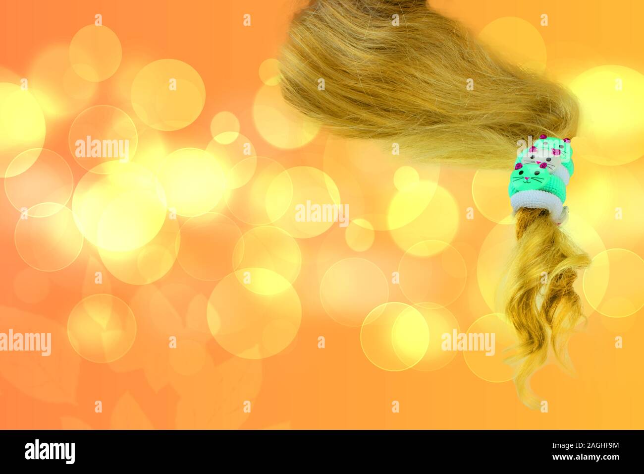 Ponytail hair holder. Closeup of three cute elastic fabric hair bands in shape of cats for kids on a piece of blonde hairs against abstract blurred go Stock Photo
