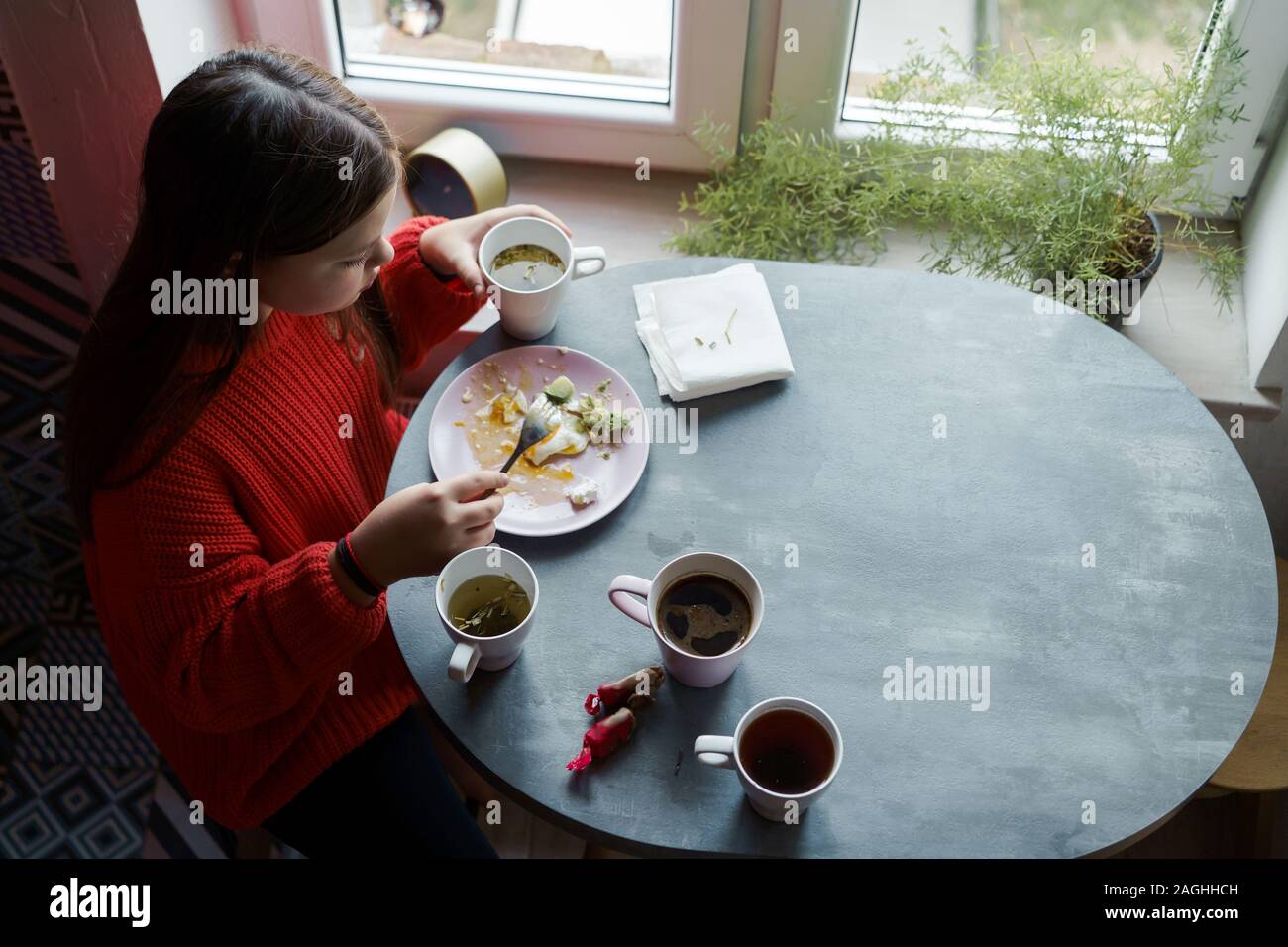 Blonde girl with long hair in a red sweater sitting at the dining table Stock Photo