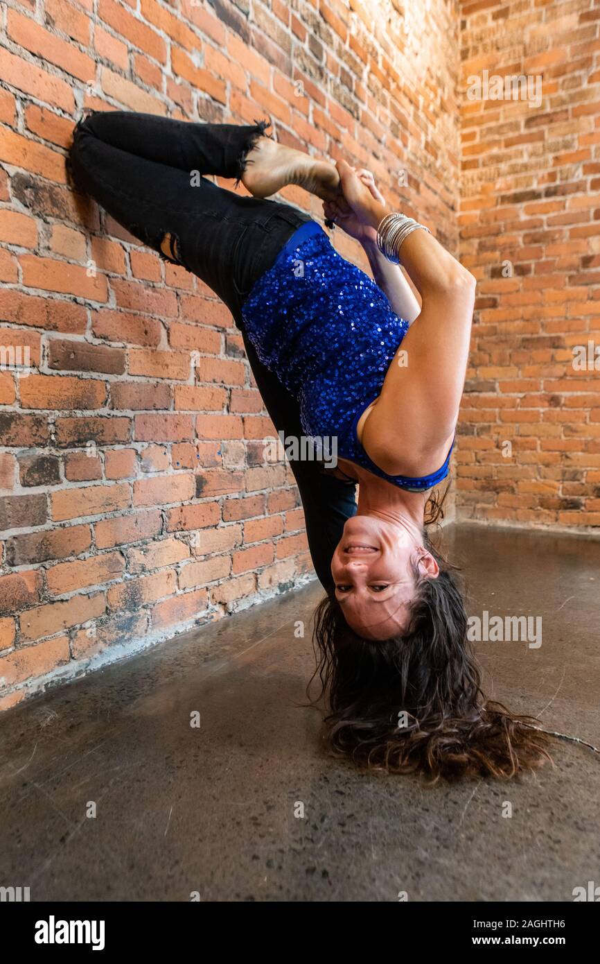 A gleeful lady is seen with her head upside down in an advanced yoga