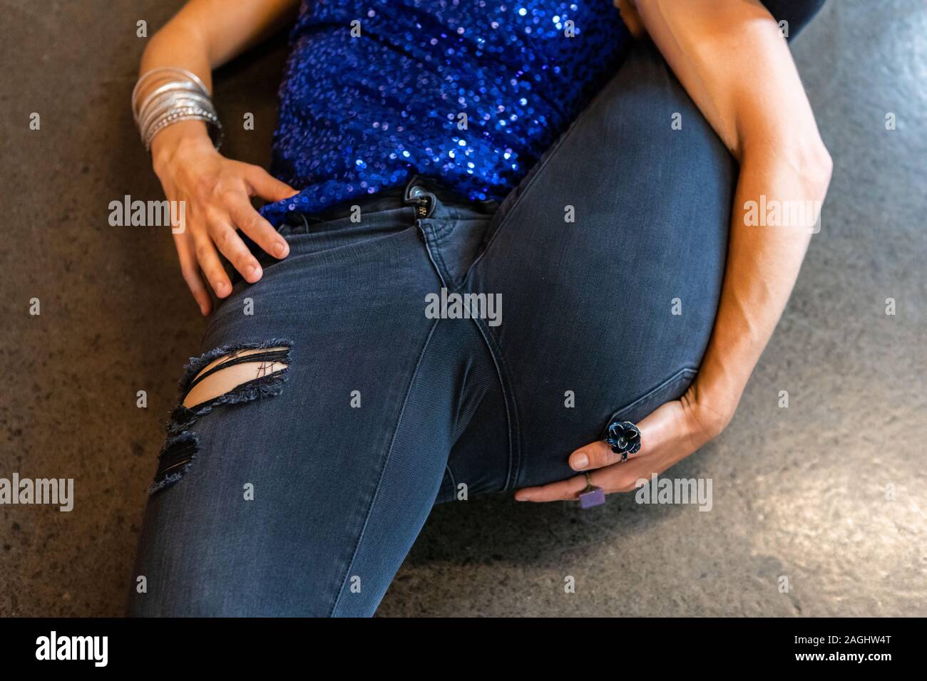 A close up shot on the thighs of a healthy woman wearing tight dark blue denim jeans during yoga, stretching leg upwards in an advanced posture Stock Photo