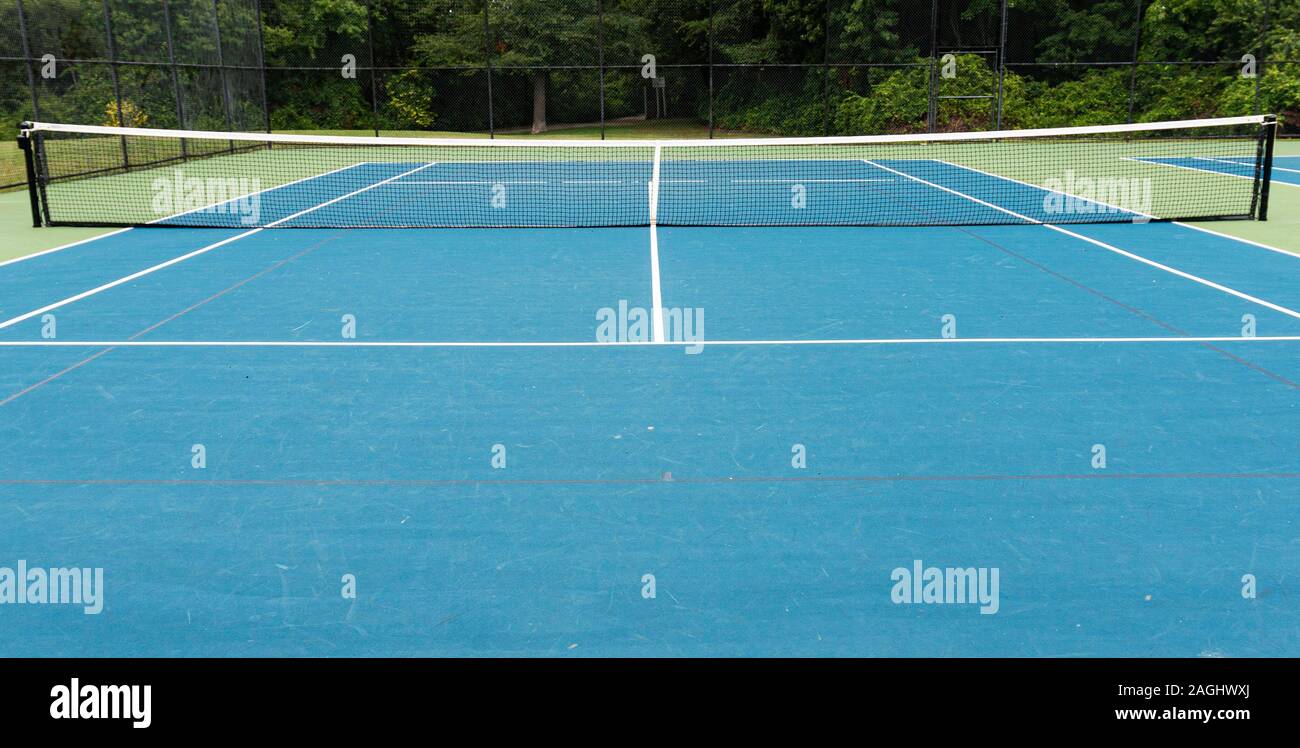 A neighborhood tennis court with a tall black fence surrounded by trees