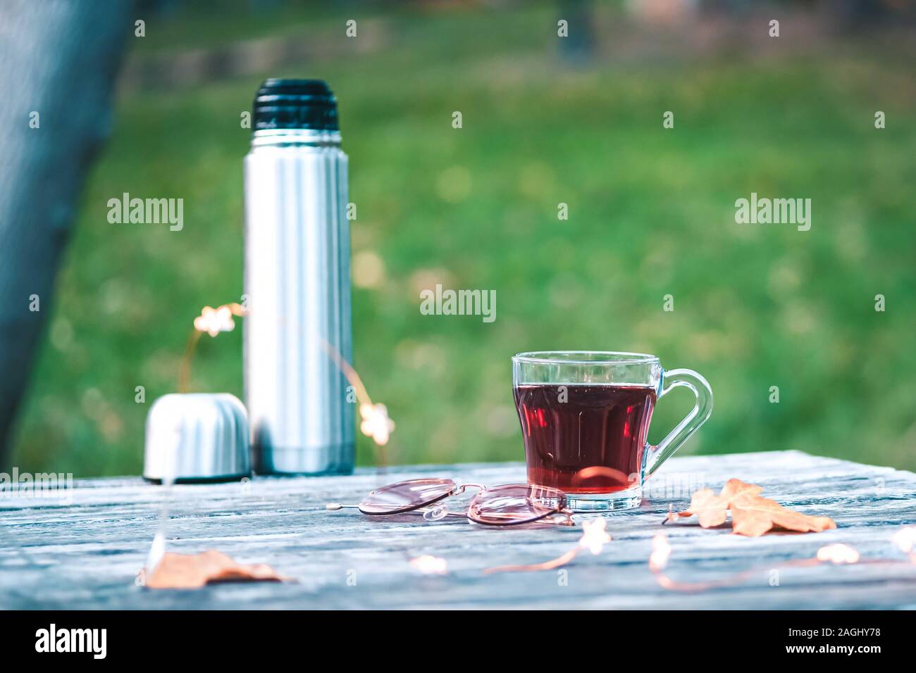 Cozy autumn or winter tea break with a cup of tea , sunglasses, christmas lights and dry autumn leaves on old vintage wooden table. top down view. Stock Photo
