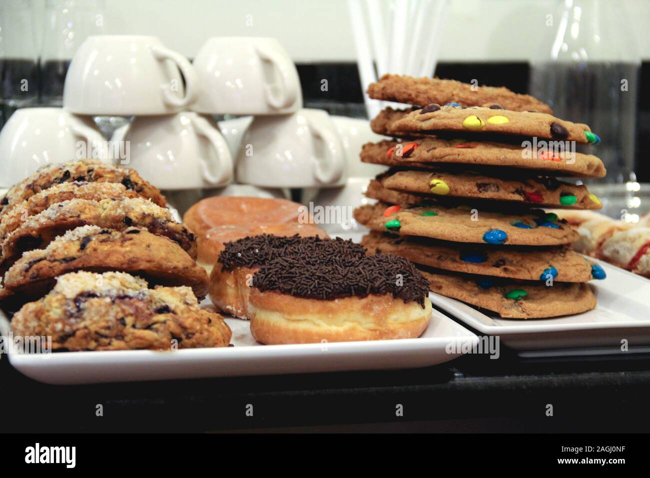 Scones, donuts, and cookies stacked in front of mugs in a coffeeshop Stock Photo