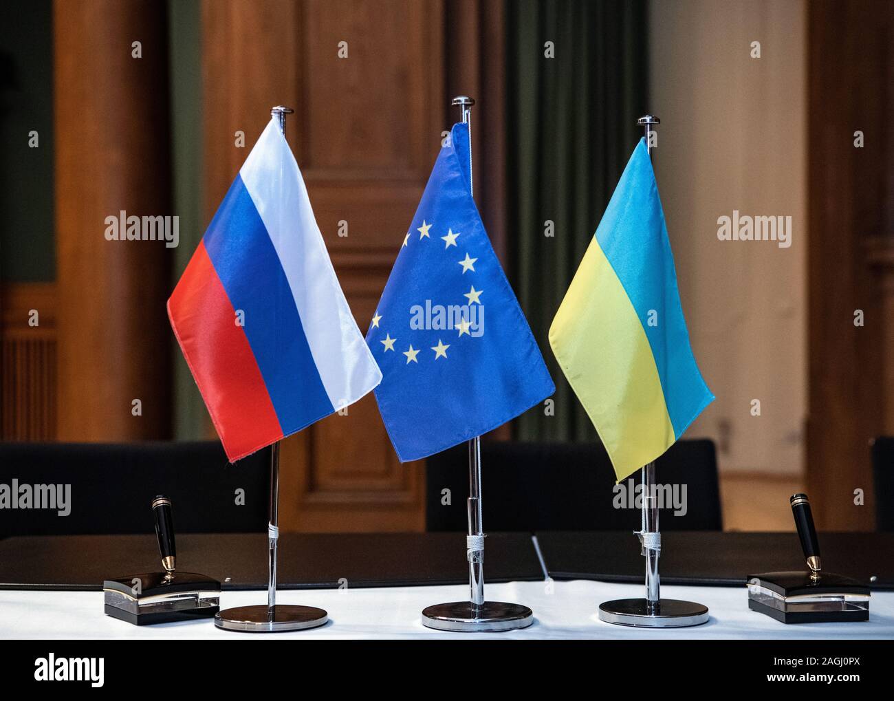 19 December 2019, Berlin: The flags of Russia (l-r), the EU and Ukraine, are on a table in the Ministry of Economy before a press conference after negotiations between Russia and Ukraine mediated by the EU and Germany. Russia and Ukraine have reached an agreement in principle on a new gas transit contract. Photo: Paul Zinken/dpa Stock Photo