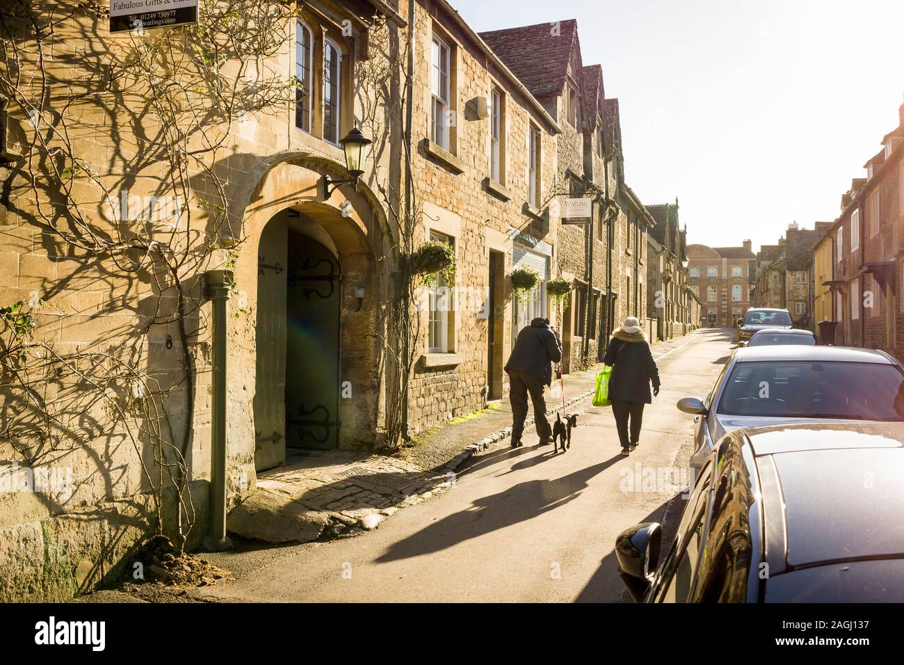 A couple with a thethered dog walking up East Street in Lacock