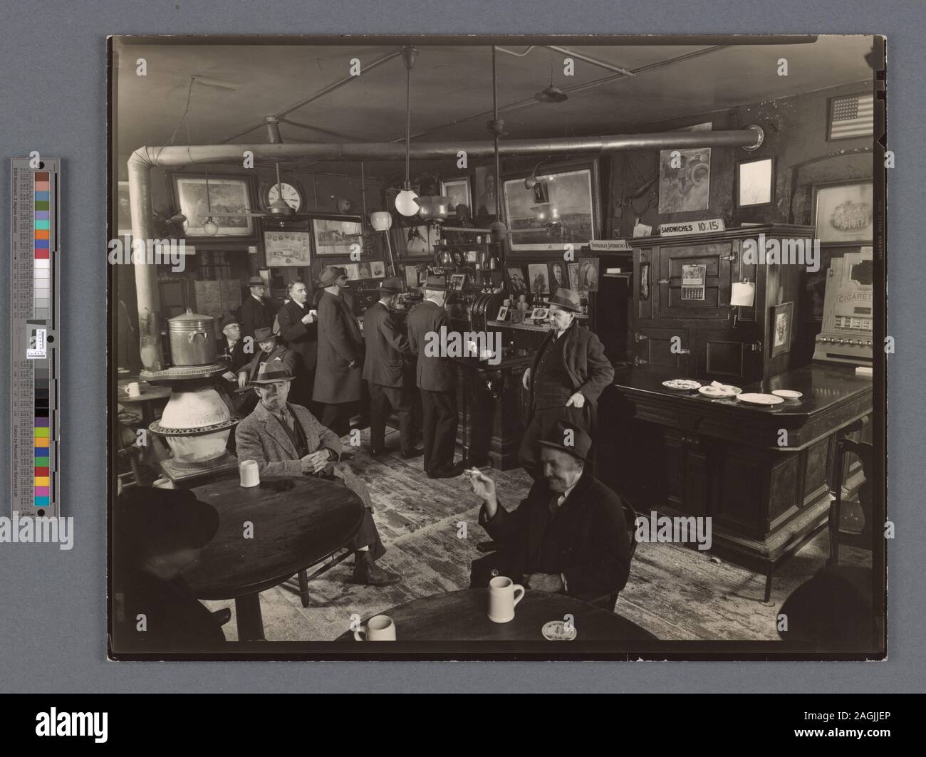 Men stand at bar, sit near stove in barroom, sawdust on the floor, pictures on the wall, food on bar near cigarette machine. Citation/Reference: CNY# 258; McSorley's Ale House, 15 East 7th Street, Manhattan. Stock Photo