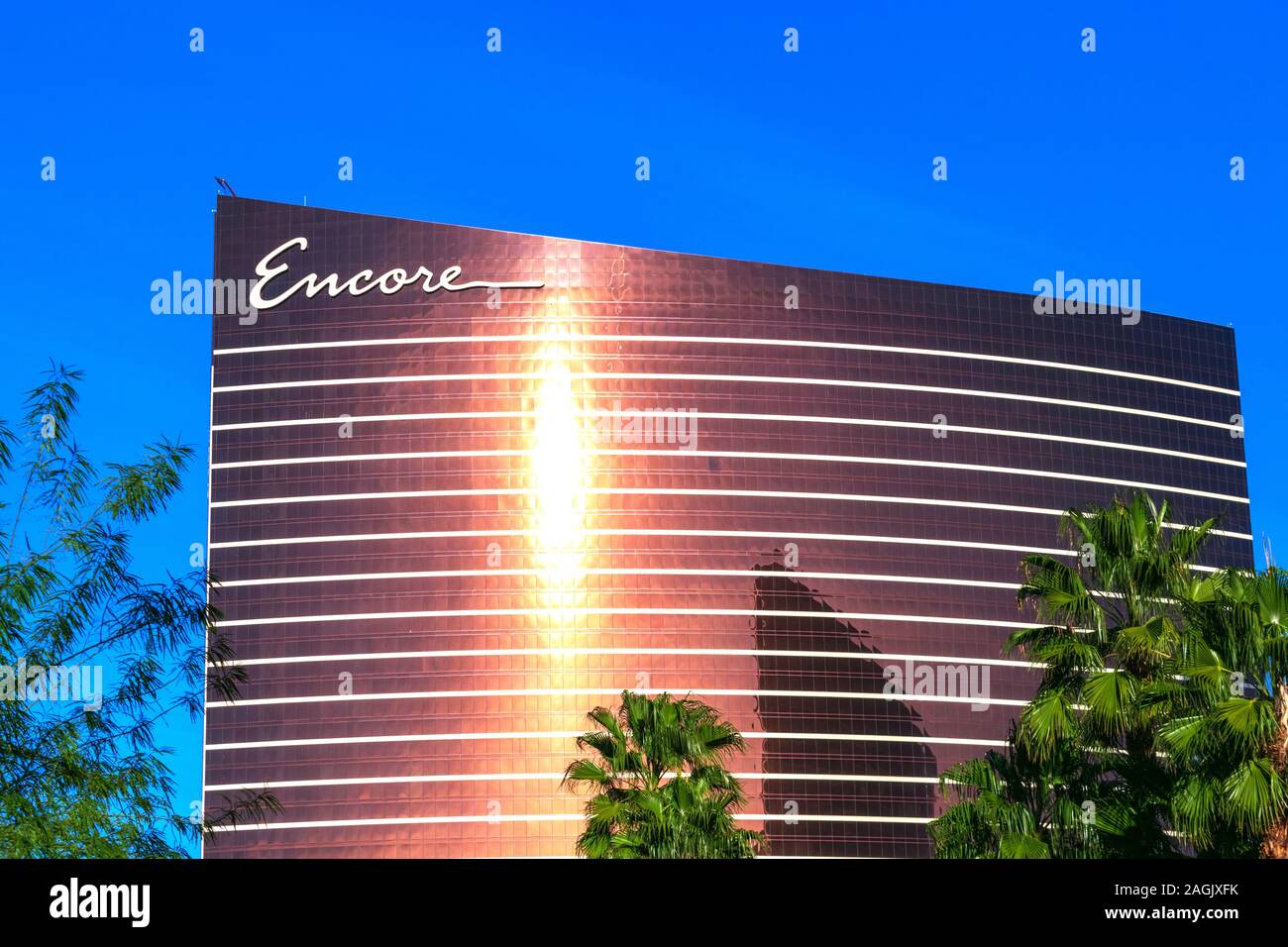Bright sunlight reflects in the modern facade of Encore luxury hotel and casino. Beautifual green palm trees in the foreground - Las Vegas, Nevada, US Stock Photo