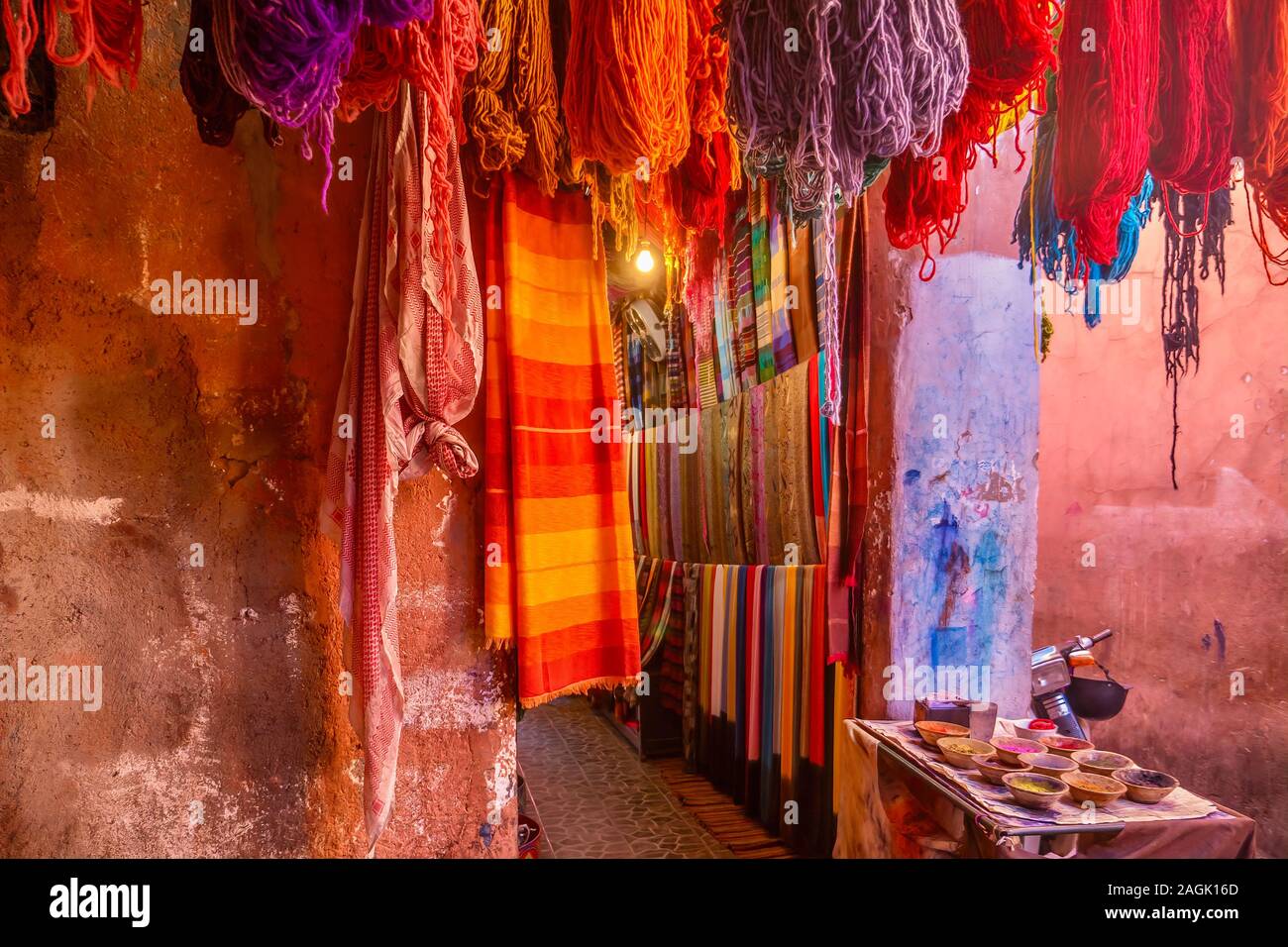 Vibrant color outside a tourist shop in Morocco, with colorful scarves, yarn and paint pigment on textured walls. In the medina of Marrakech. Stock Photo