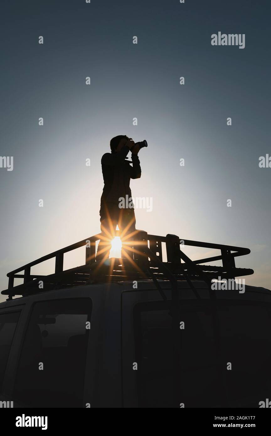 Woman takes pictures standing on car roof rack. Contre jour picture. Image for travel and adventure layouts Stock Photo
