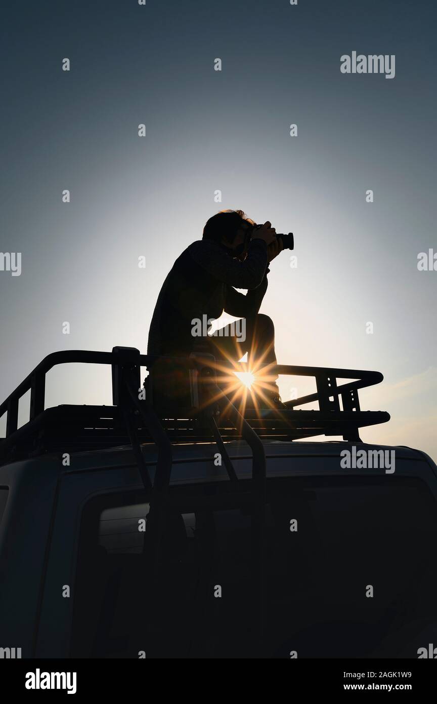 Photographer takes pictures standing on car roof rack. Contre jour picture. Image for travel and adventure layouts Stock Photo