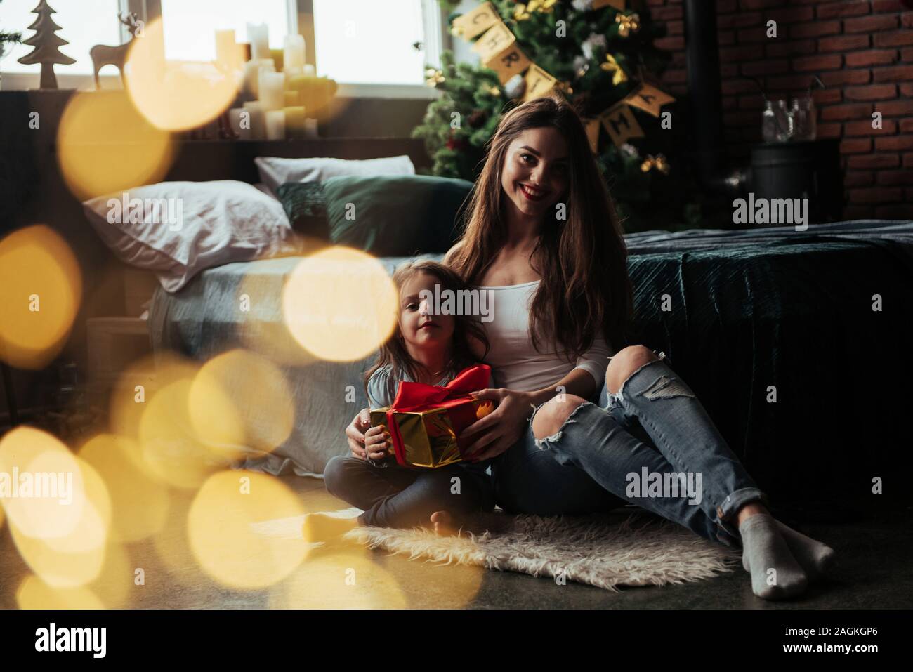 Nice portrait. Mother and daughter sits in holiday decorated room and holds gift box Stock Photo