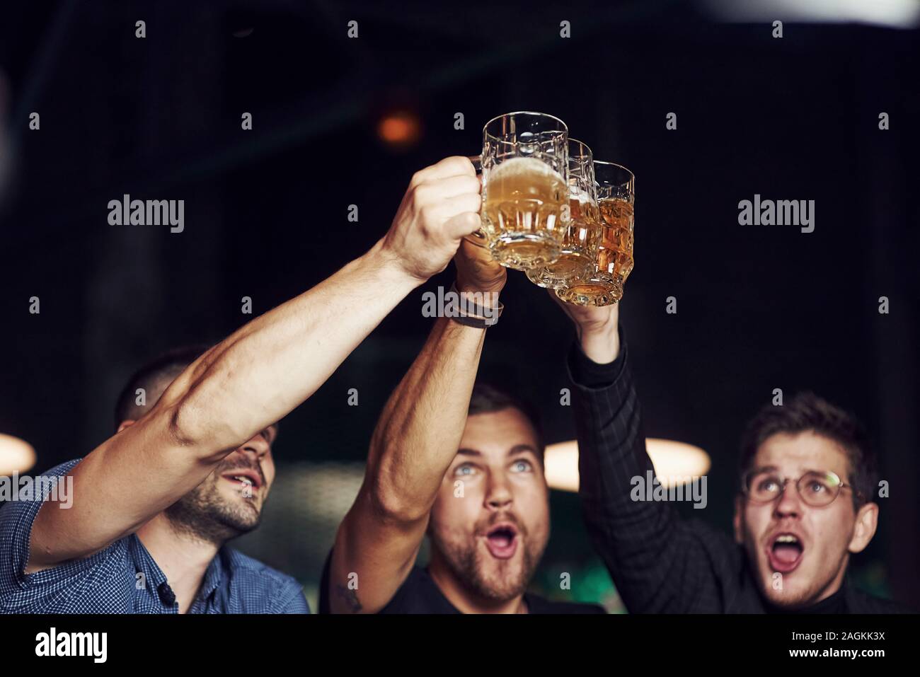 Knocking glasses. Three sports fans in a bar watching soccer. With beer