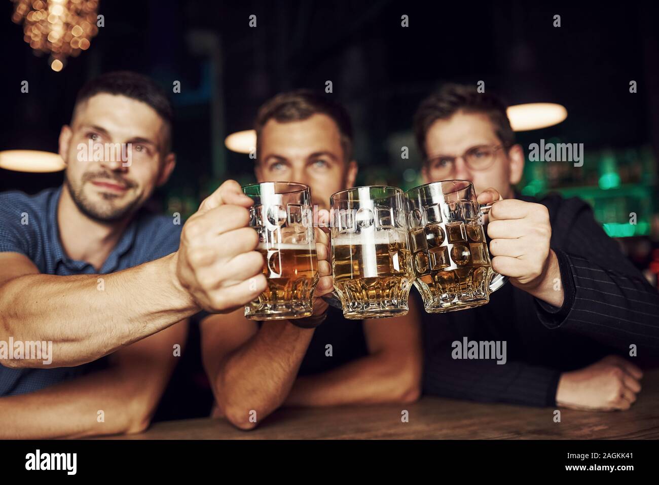 Knocking glasses. Three sports fans in a bar watching soccer. With beer