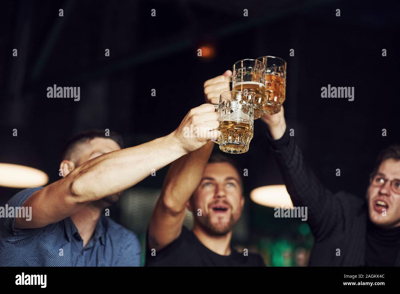 Knocking glasses. Three sports fans in a bar watching soccer. With beer