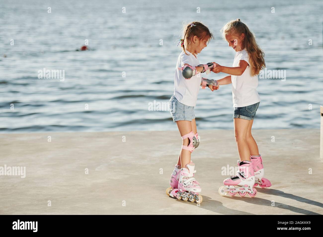 Two kids learning how to ride on roller skates at daytime near the lake