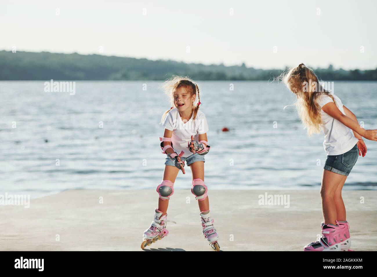 Two kids learning how to ride on roller skates at daytime near the lake