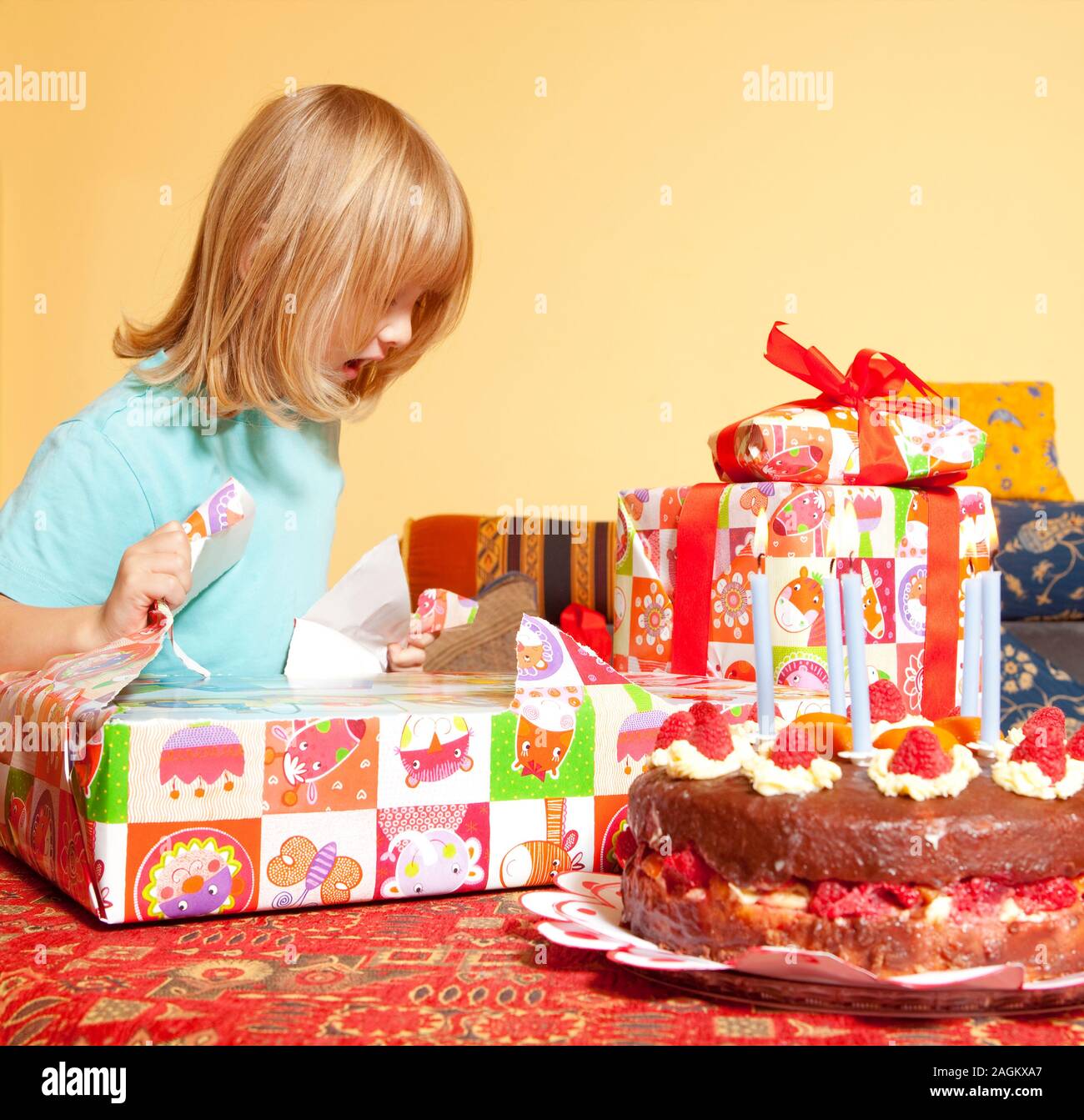 boy with long blond hair opening his birthday presents Stock Photo