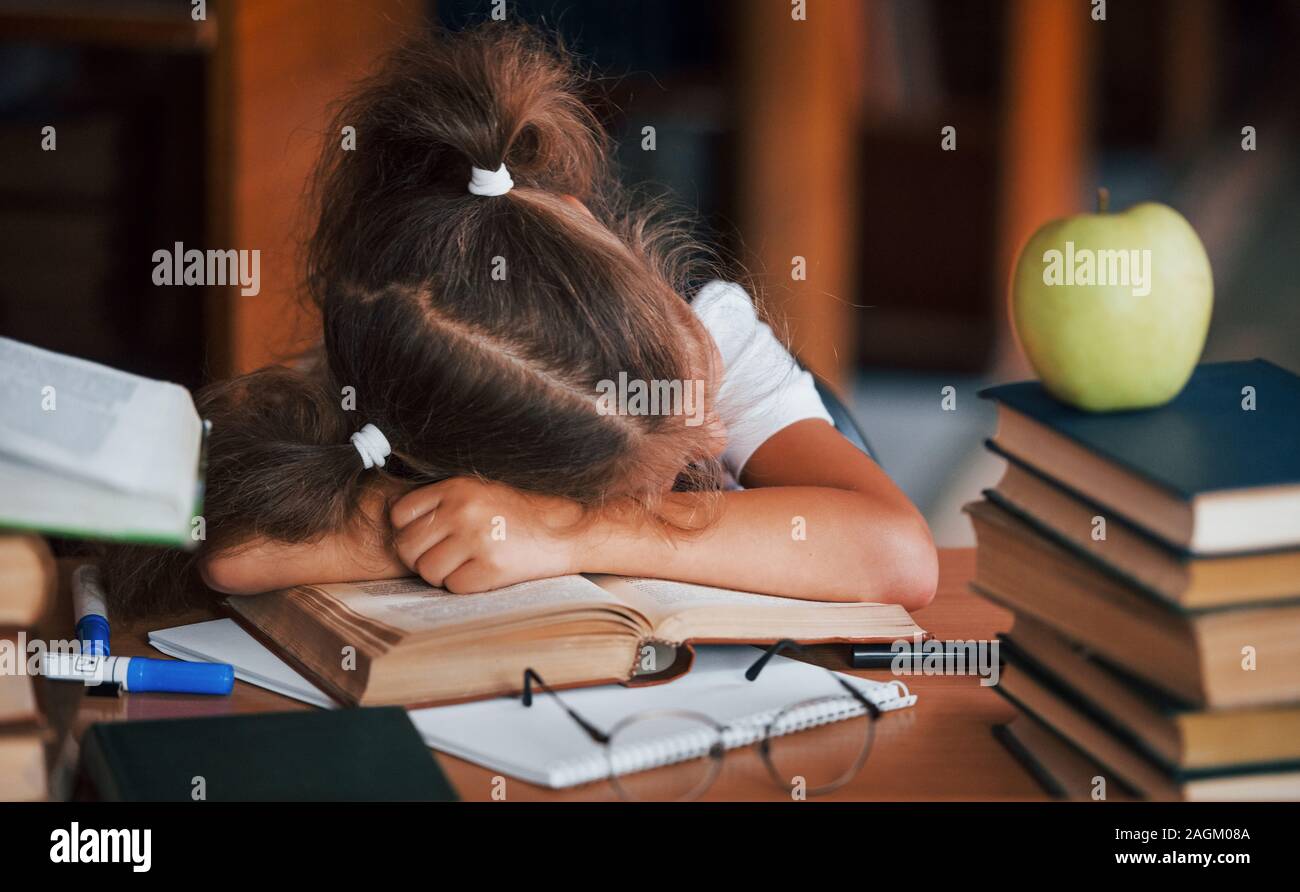 Sleeping on the table. Cute little girl with pigtails is in the library. Apple on the books Stock Photo