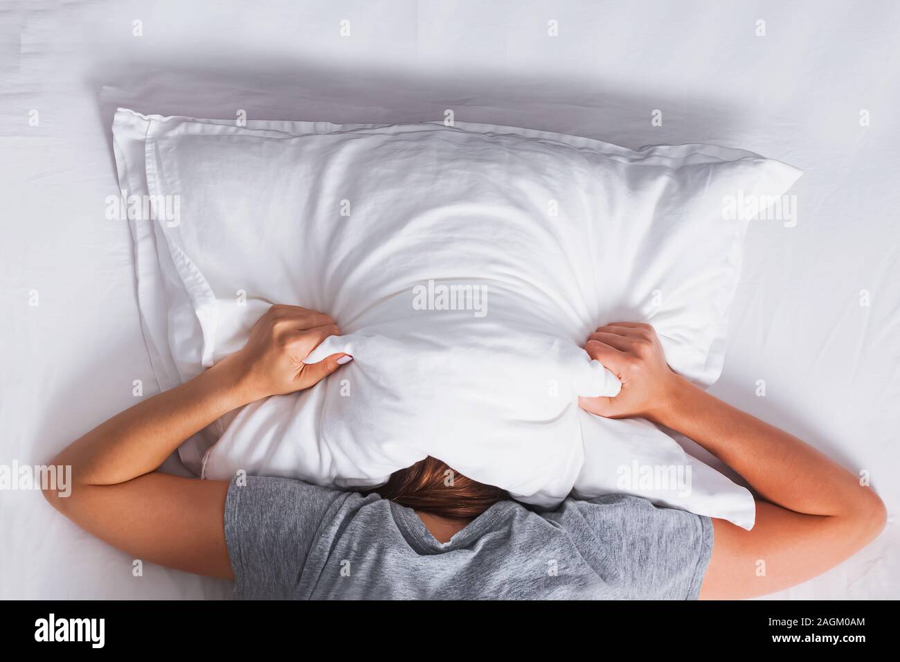 Woman lying on the bed and covering her head with pillow Stock Photo