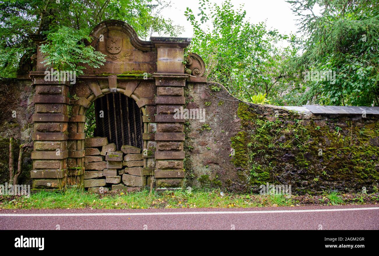 A partially blocked up gateway in a moss-covered wall guards the overgrown garden of the derelict Courthill House mansion beside the A896 road at Kish Stock Photo