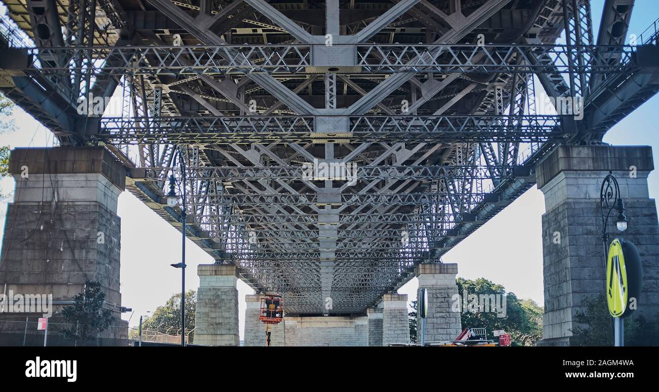 A underneath view of the structure of the Sydney Harbour bridge made up of steel beams and girders sat on concrete Granite faced pillars Stock Photo