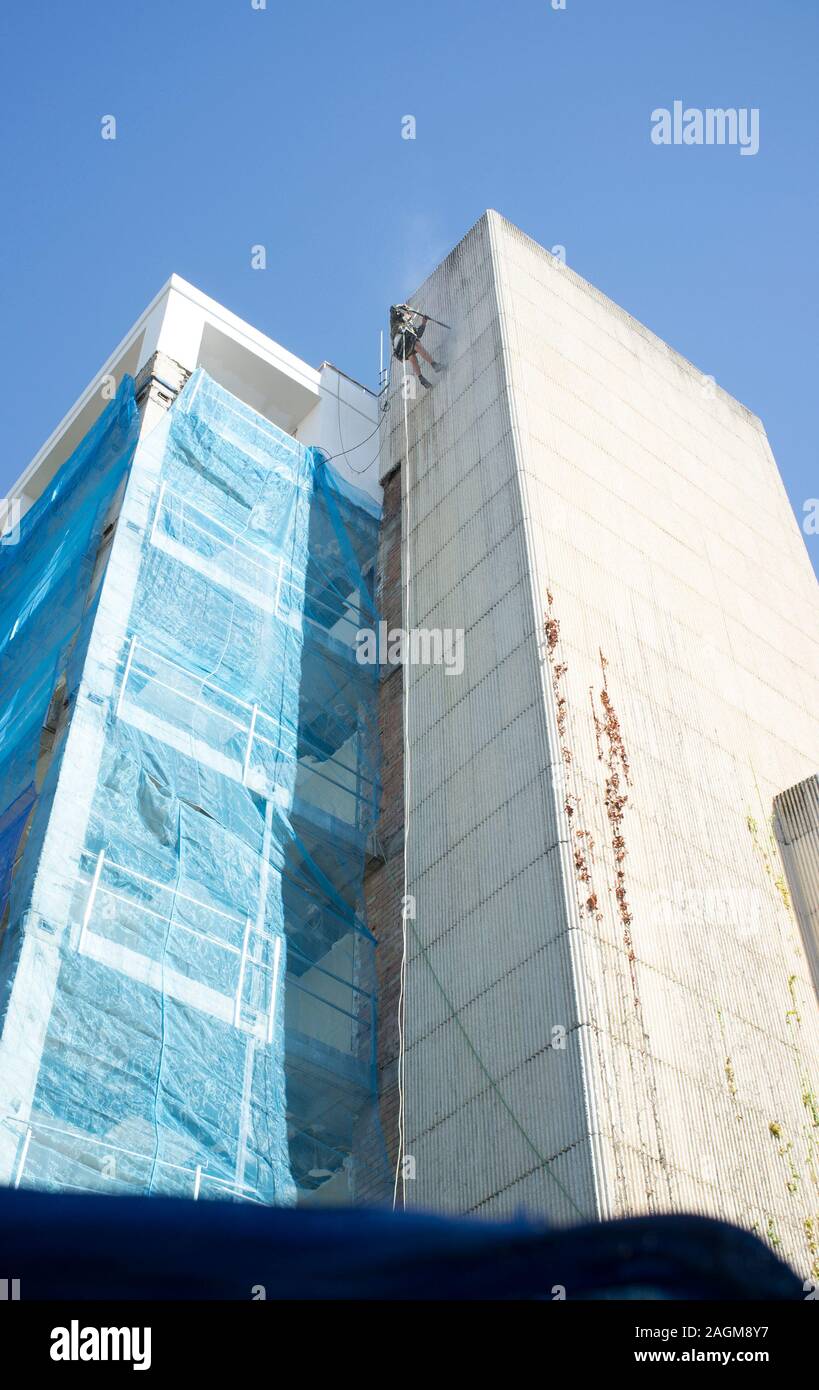 Rope access technician washing building facade. Cleaning service at height concept Stock Photo
