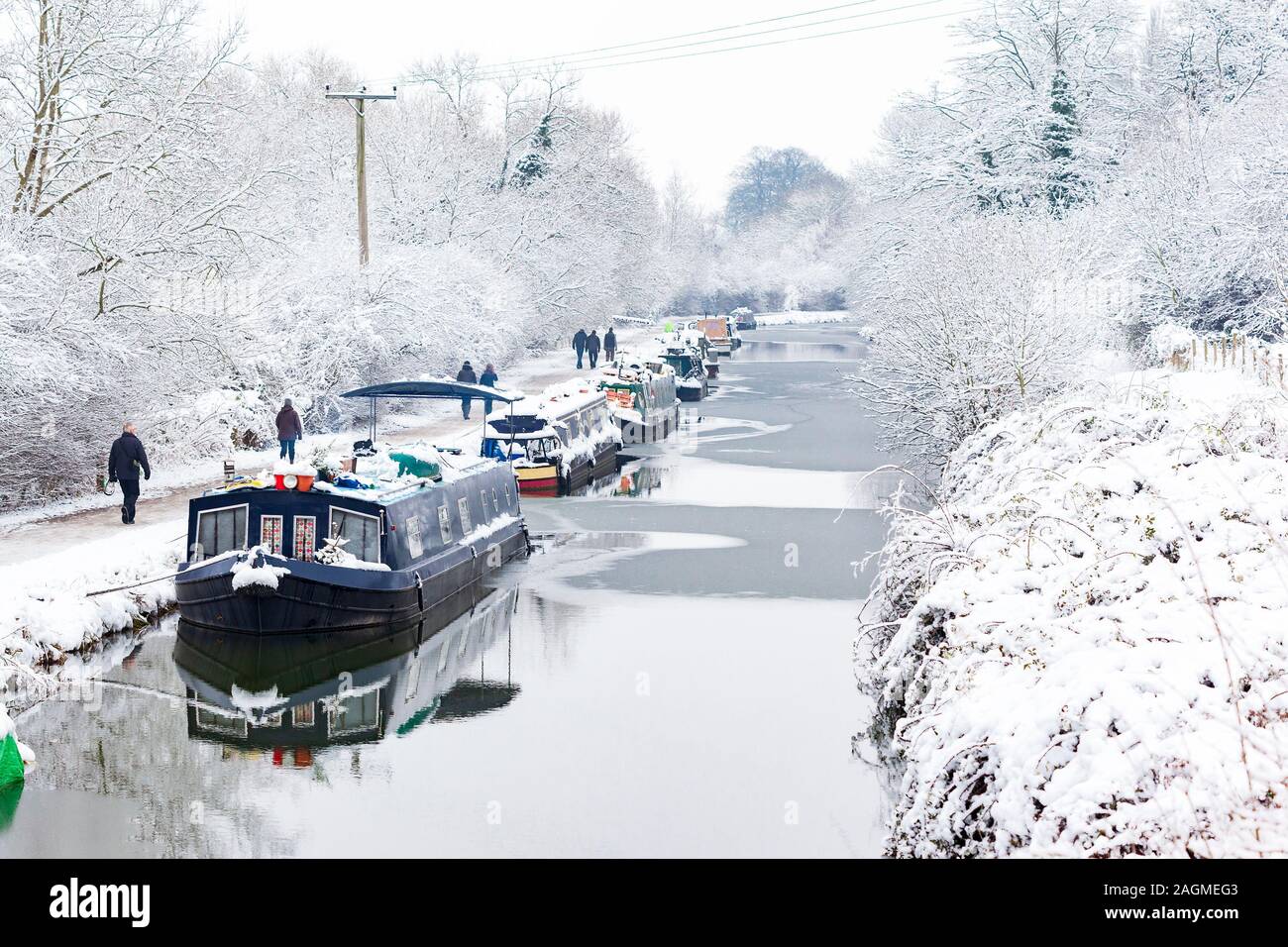BATH, UK - 19 JAN : Walkers pass moored boats on the Kennet and Avon canal in the snow on 19th Jan 2013. The boats stay moored throughout the winter Stock Photo