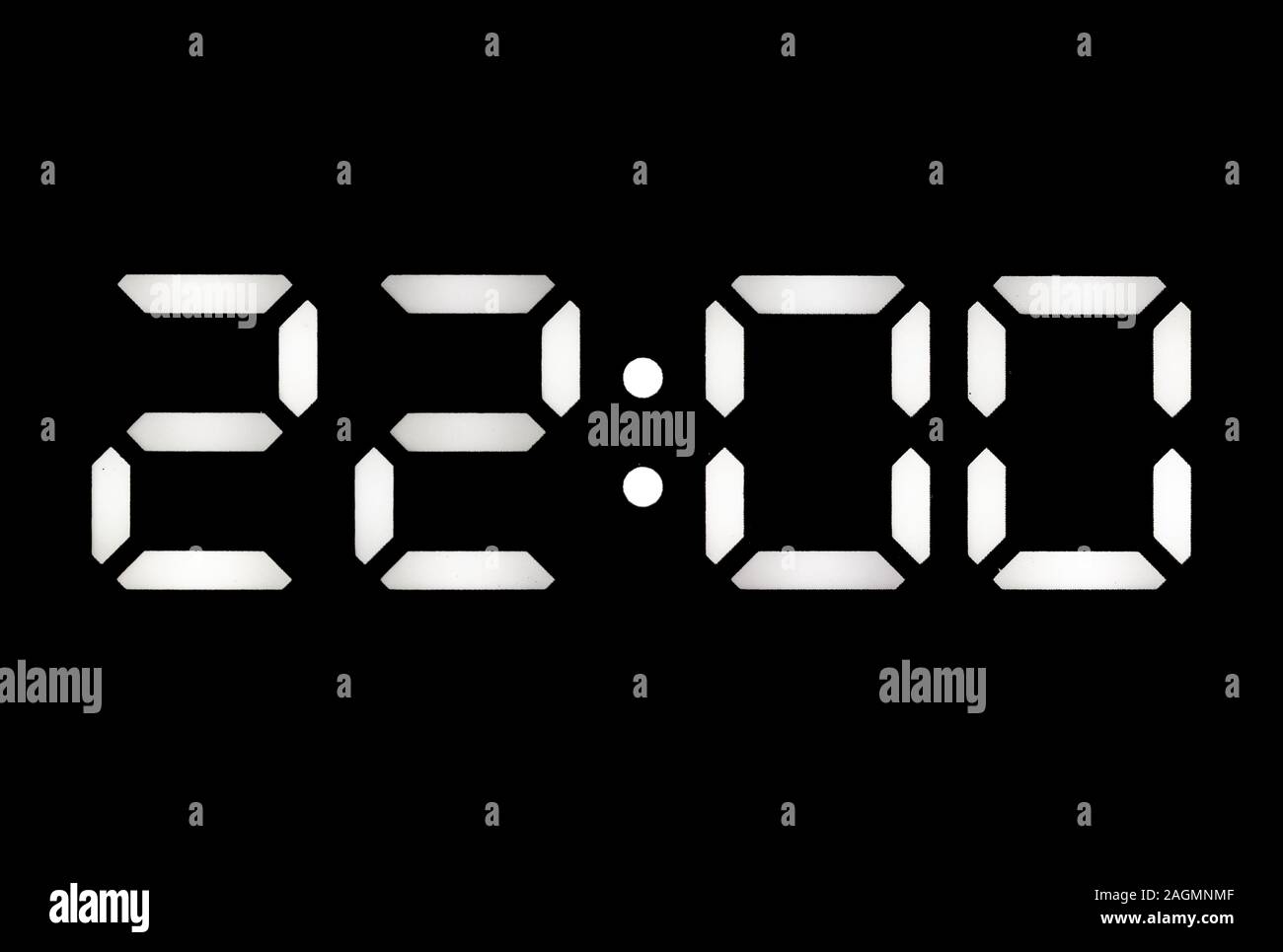 Real white led digital clock on a black background showing time 22:00 Stock Photo