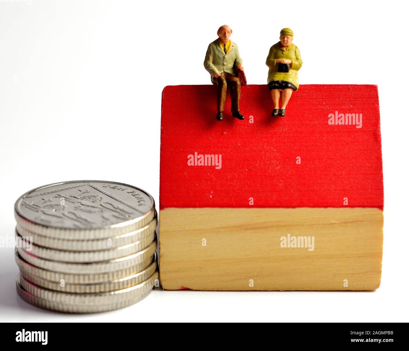 Equity release concept,miniature pensioner figurines sitting on a house next to silver coins Stock Photo