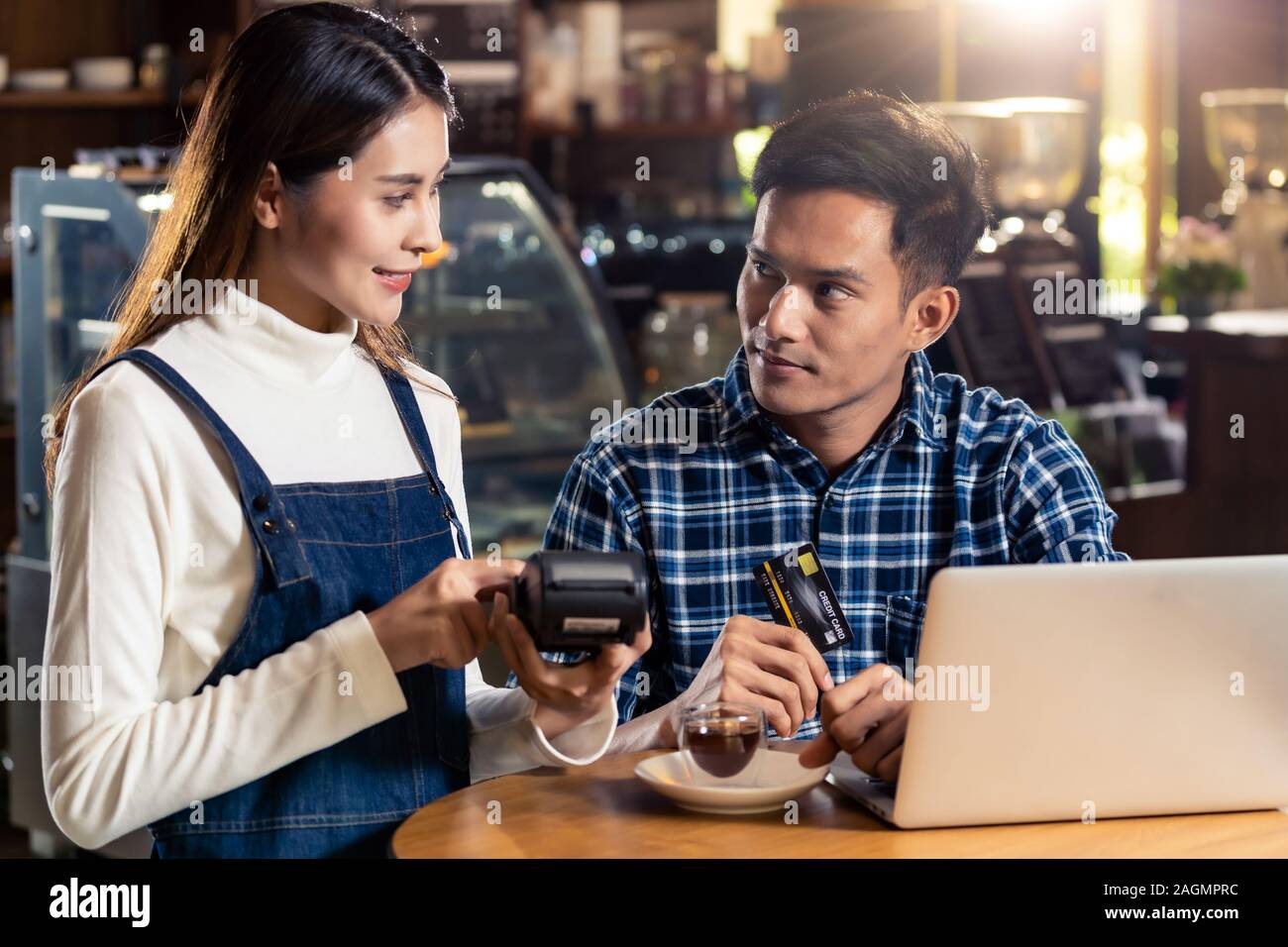 Asian customer using credit card with contactless nfs technology to pay a waitress for coffee purchase at table in cafe. Stock Photo