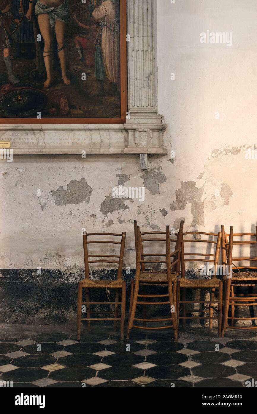 Wooden simple chairs and legs of an old painting detail in the interior of Saint Andrew's Church in Levanto, La Spezia, Liguria, Italy EU Stock Photo